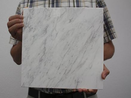 Osoba drží před kamerou bílou mramorovou dlaždici s šedými žilkami.