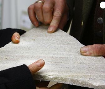 Dvě ruce drží kus přírodního kamene z taunského kvarcitu