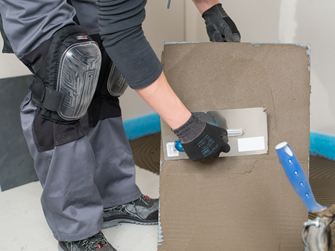 Obkladač nanáší lepidlo na zadní stranu dlaždice.