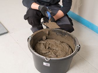 Obkladač před kbelíkem s lepidlem na přírodní kámen