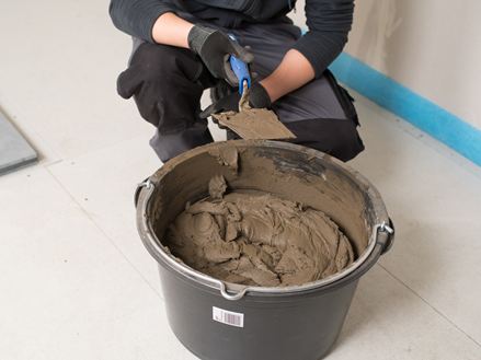 Obkladač před kbelíkem s lepidlem na přírodní kámen