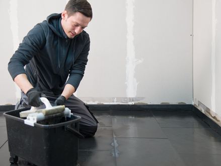 Obkladač klečí na položené břidlicové podlaze a smývá přebytečnou spárovací hmotu.