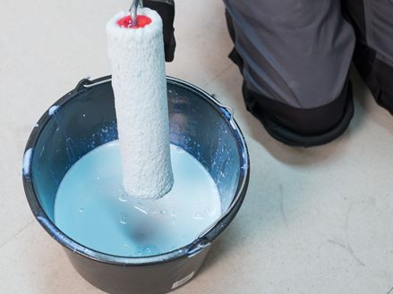 Obkladač namočí váleček do kbelíku s nátěrem