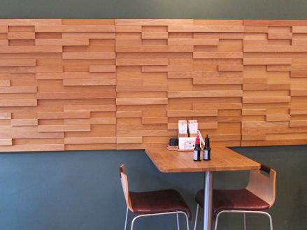 Stůl se dvěma židlemi před šedou stěnou s hnědým dřevěným obložením v bistru.